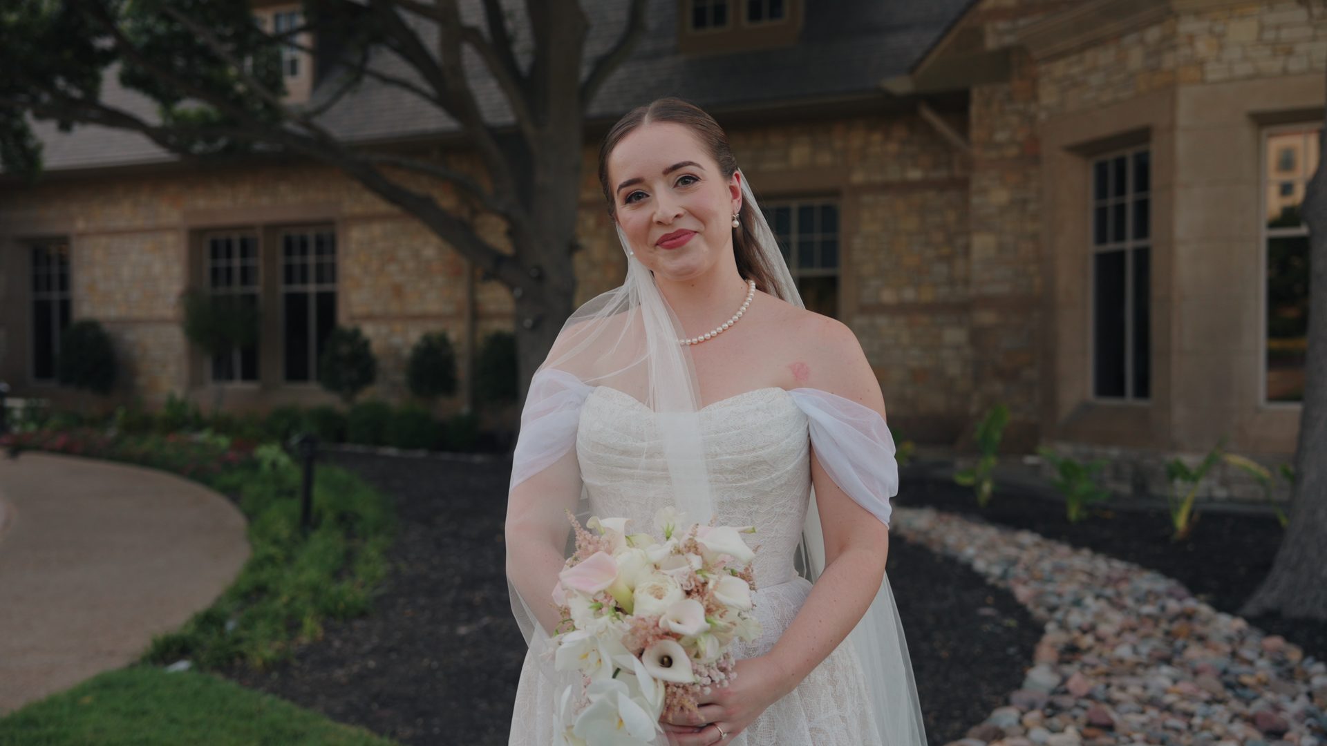 A bride smiling with her bouquet outside the clubhouse at Stonebriar